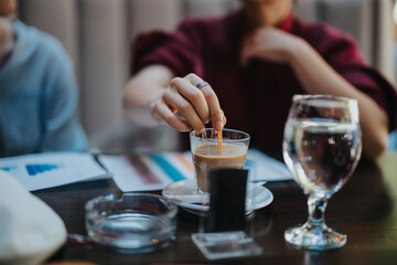 Businesspeople engaging in a meeting at a coffee shop, discussing work while enjoying drinks and reviewing documents.
