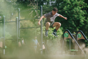 Young man jumping on outdoor fitness equipment performing a calisthenics workout in the park. Active lifestyle, exercise, and strength training.