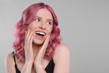 Happy girl with pink hair on grey background, space for text