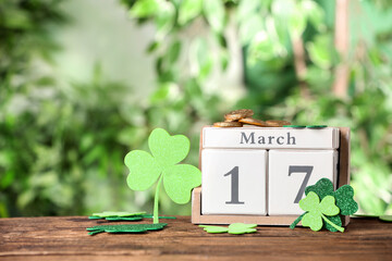 Composition with block calendar on wooden table against blurred greenery, space for text. St....