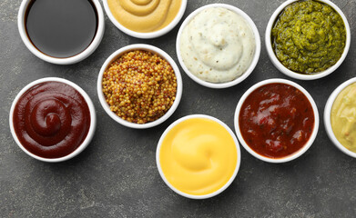 Many different sauces in bowls on grey table, top view