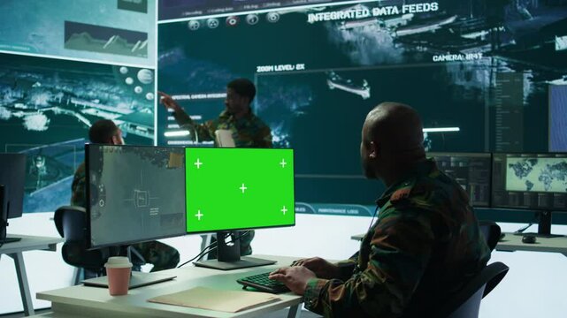 Soldier analyzing real time data next to green screen in high tech military office, processing intelligence for field operations and coordinating strategic missions to ensure national interests