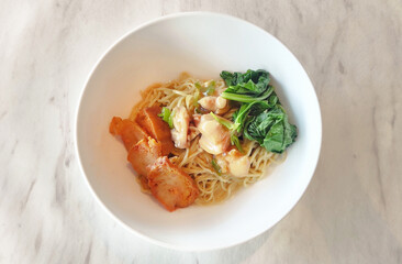 chicken noodles topped with crispy fried chicken kekian, green mustard leaves, doused with thick sauce, served in a white bowl isolated on a gray patterned putoh marble stone background