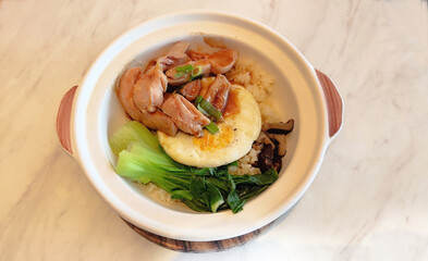 healthy Chinese food consisting of chicken fillet, fried egg, green mustard greens and mushrooms served with white rice in a ceramic bowl with a wooden coaster isolated on white gray marble stone