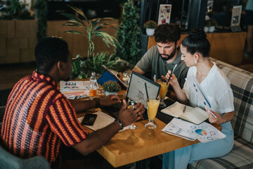 Diverse group of people having a collaborative meeting in a cozy coffee shop environment. Discussing charts and data while enjoying beverages.