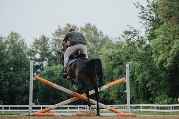 Rear view of a horse rider jumping over a hurdle in an outdoor equestrian competition....