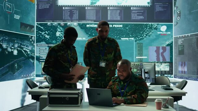 Military personnel in a modern command center handle critical information, collecting live surveillance data to maintain security protocols. Team of army crew working on reconnaissance. Camera B.