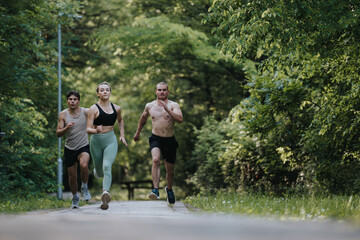 Fototapeta premium Three athletes running on a pathway in a green park, showcasing fitness, endurance, and active lifestyle.