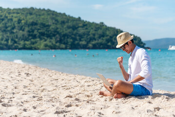 Man traveler use laptop on summer beach blue sky. Asian man casual blue short pants white shirt relax sitting summer beach. Man typing laptop computer holiday business trip freelance work on island