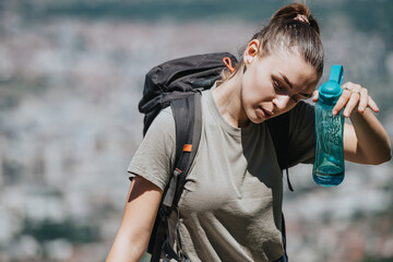 Young woman exploring nature and staying hydrated while hiking in the mountains, showcasing the...