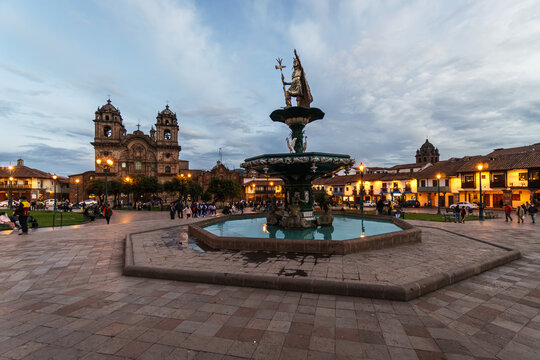 Cusco, Peru: Inco emperor topped fountain in the middle of the plaza de armas in Cusco colonial old town at dusk with the Church of the Society of Jesus in Peru in the Andes