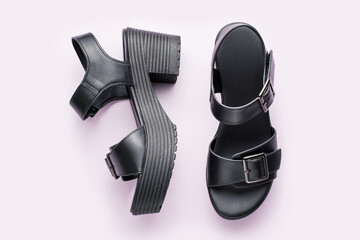 Female leather black sandals on the platform close-up on pink background.