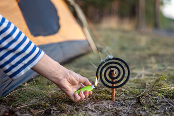 Cropped hand with lighter igniting repellent coil fumigator with smoke for repelling insects in...