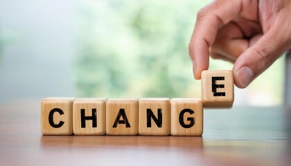 A hand is holding a wooden block with the letters CHANGE written on it. The block is being broken into pieces, symbolizing the idea of change