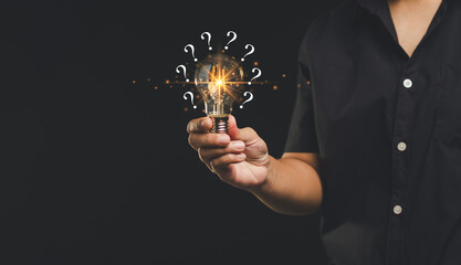 Person holding illuminated light bulb with question marks, symbolizing ideas.