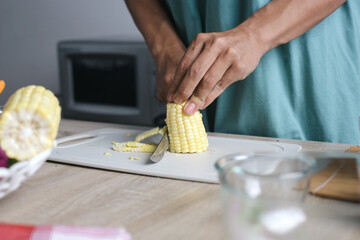 Man Using Knife Cuts Corn Kernels From The Cob On Cutting Board