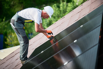 Worker building photovoltaic solar panel system on rooftop of house. Man engineer in helmets and...