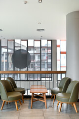 Comfortable seating area with green chairs and small round tables near large windows.