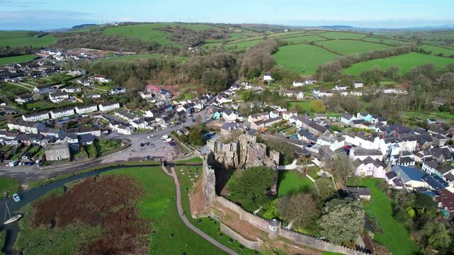 Drone over Coran River towards Laugharne Castle with town and green meadows, Wales