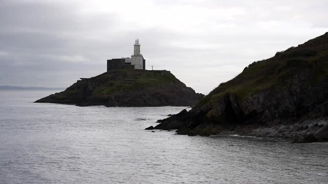 Old white Mumbles Lighthouse on small island during high tide and overcast day in Bracelet Bay, Wales