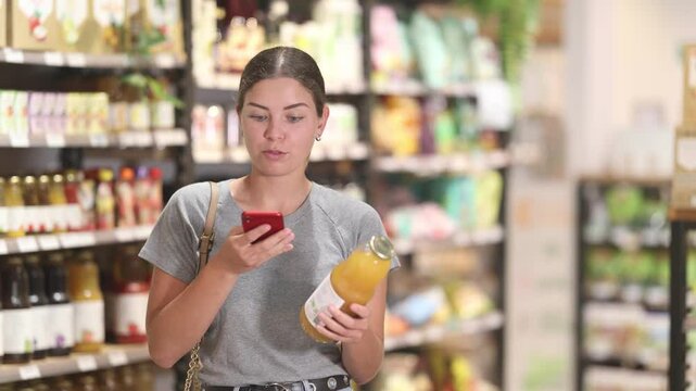 Young woman in supermarket scan QR code bottle of drink. Girl buyer photo information on packaging of bio product. 