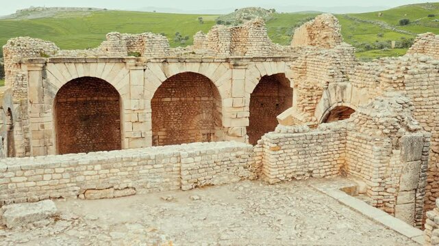 Weathered remains of Grand Nymphaeum in Dougga, historic Roman archaeological site in Tunisia, with stone archways under clouded spring sky
