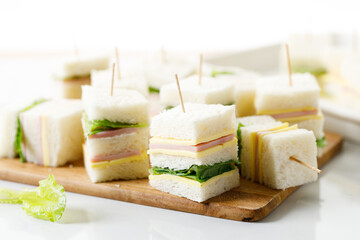 Sandwich of white soft bread with ham, cheese and lettuce on wooden board.
