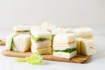 Sandwich of white soft bread with ham, cheese and lettuce on wooden board.