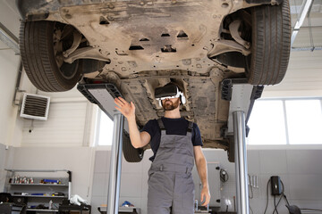 Mechanic examining technical condition of car on lift with using virtual glasses in workshop. Innovative use of VR technology for automotive diagnostics and repair enhancement