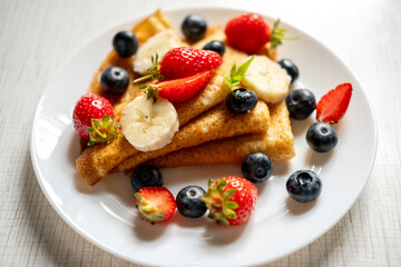 Delicious appetizing pancakes with strawberries, blueberries and banana on a white plate.