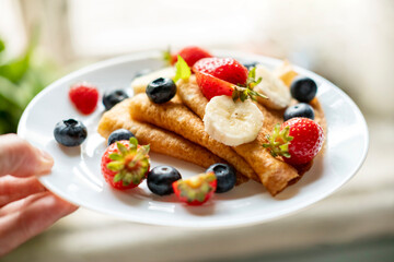 A man's hand holds a plate of delicious and appetizing pancakes with berries.