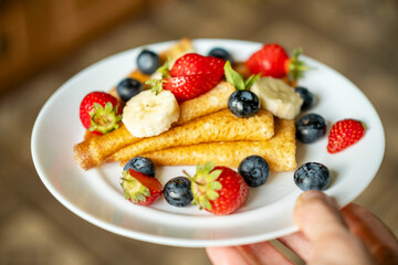 Plate with sugarless rye flour pancakes decorated with berries in a man's hand.