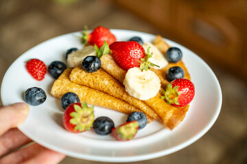Plate with sugarless rye flour pancakes decorated with berries in a man's hand.