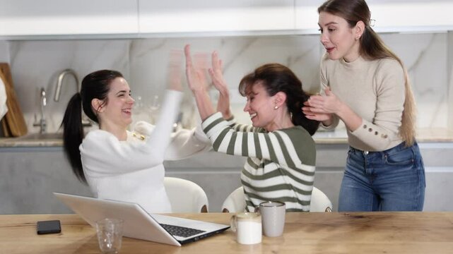 Three happy middle-aged woman expressing joy for winning standing by laptop at home. High quality 4k footage