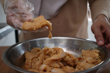 Close up of a person hand marinating chicken meat in metal bowl