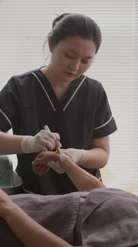 Vertical shot of Asian female beautician gelling arms of female client during procedure of IPV epilation