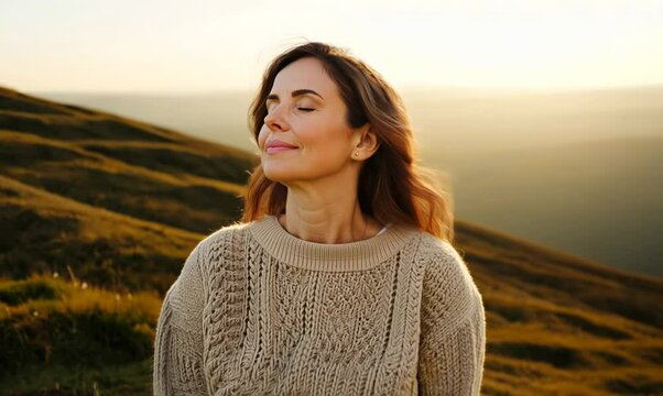Medium shot portrait video of a woman in her 40s practicing mindfulness sophrology relaxation & stress-reduction wearing a cozy sweater against a hillside or rolling hills background