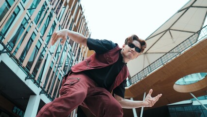 Low angle of asian attractive hipster pose at camera surround by mall. Portrait of break dance choreographer looking at camera while dancing in hip hop style. Outdoor sport 2024. Hiphop.