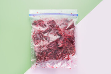 Ziplock cellophane bag with frozen and sliced beets on a green and pink background top view...