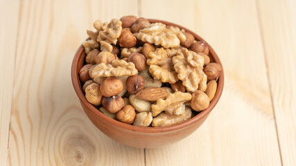 Mixed nuts in a clay cup on a wooden table, walnut kernels, peeled dried hazelnuts, almonds and...