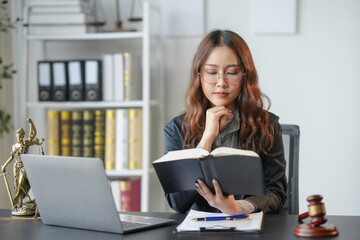 Lawyer is sitting at her desk reading a law book, preparing for a case. She is wearing a suit and glasses and has a thoughtful expression on her face