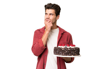 Young caucasian man holding birthday cake over isolated background having doubts