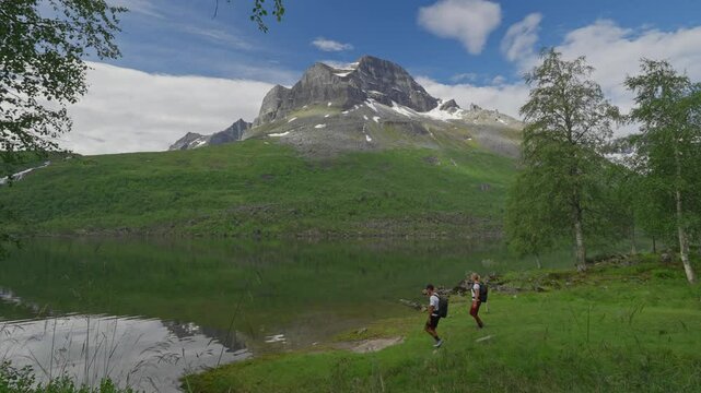 Two hikers explore the scenic Innerdalen valley in Norway, surrounded by lush greenery and a serene lake