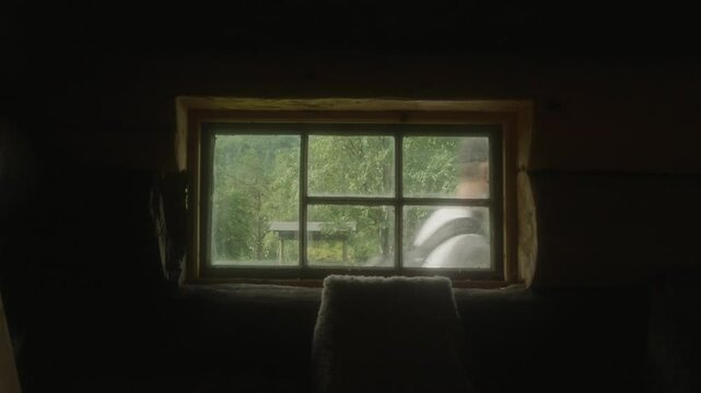 A cozy cabin window offers a view of two hikers and lush greenery in Innerdalen, Norway