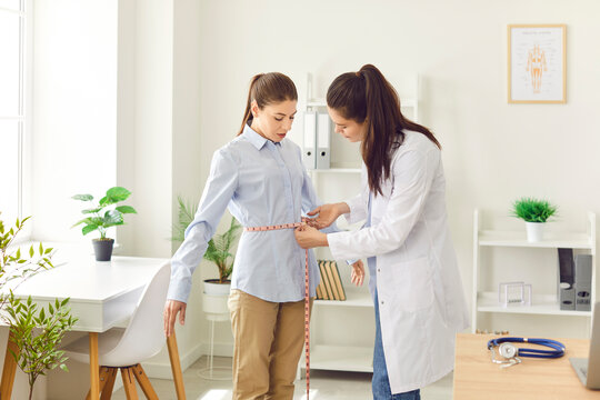 Doctor, nurse measuring young female patient waist line with tape during check up in clinic, medical exam for weight loss healthy dietary, regular medical physical examination, overall body health 