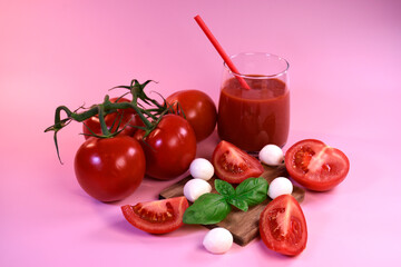 A glass of tomato juice with fresh tomatoes, mozzarella and basil on a pink background. Healthy eating
