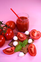 A glass of tomato juice with fresh tomatoes, mozzarella and basil on a pink background. Healthy eating