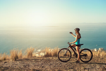 Picture, bike and woman with fitness, nature and social media with influencer, training and wellness. Healthy, person and biker with smartphone, cyclist and cardio with memory, ocean view and bicycle