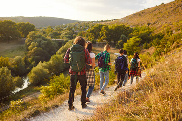 Obraz premium Backside views of a team of tourists enjoying vacation together by hiking in the mountains. Group is on a trip, making the most of leisure time by exploring nature and enjoying a hike.