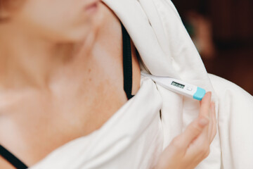 Woman in white shirt holds electronic thermometer in hand, black bra visible